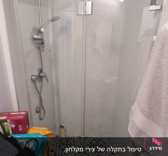 מקלחון זכוכית עם ראש מקלחת ומגבת תלויה